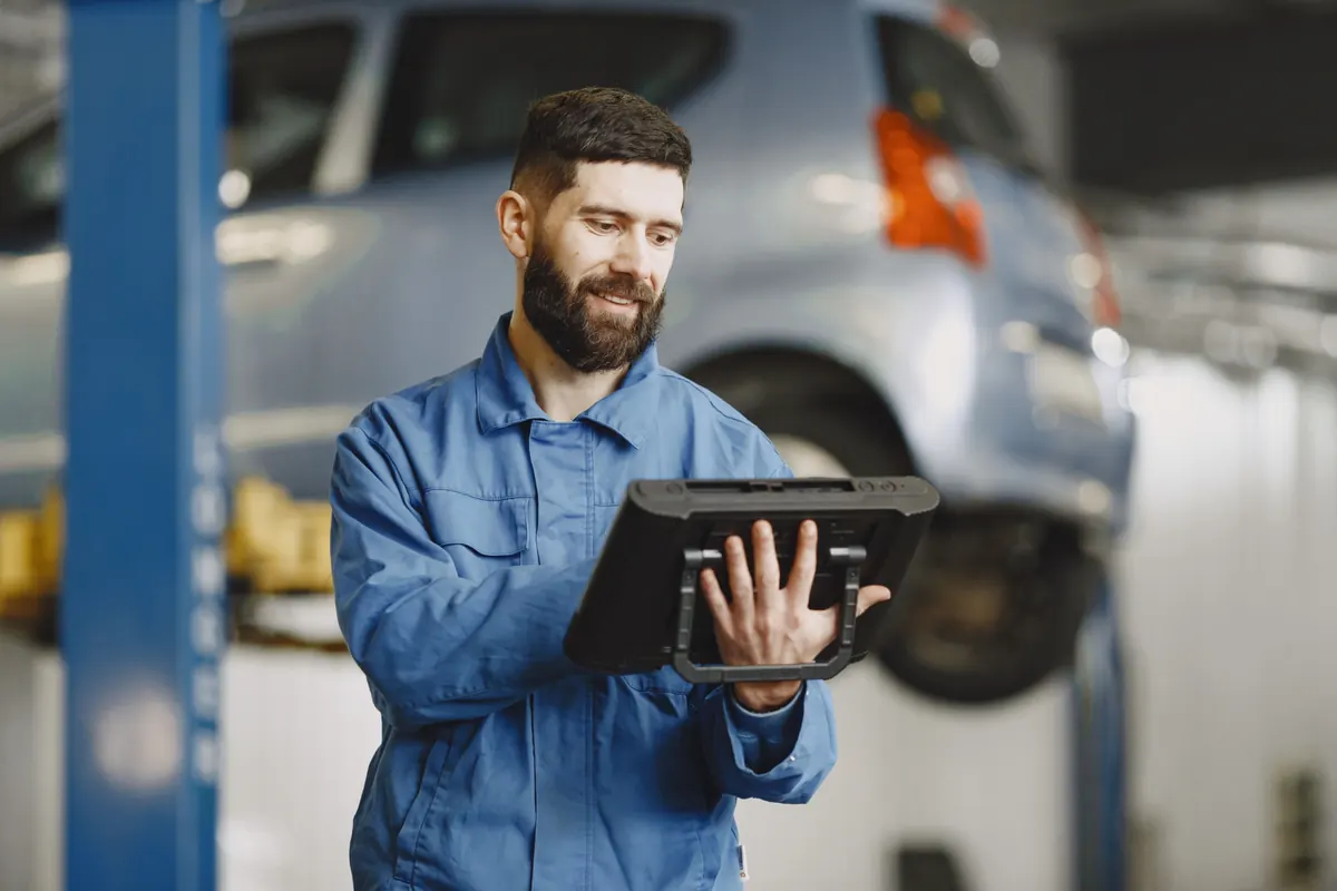 Auto mechanic in a shop reviewing service records on a rugged tablet